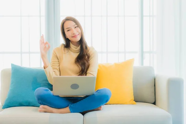 漂亮的年轻亚洲女人在客厅的沙发装饰上使用电脑笔记本电脑 — 图库照片