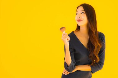 Sarı izole arkaplanda makyaj fırçası olan güzel bir Asyalı kadın portresi.