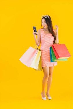 Renkli alışveriş çantalı güzel Asyalı kadın akıllı cep telefonu ve sarı izole edilmiş arka planda kredi kartı.