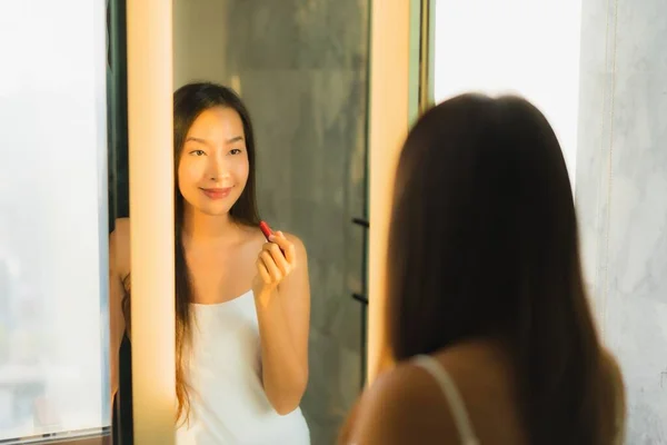 ポートレート美しいです若いですアジアの女性作るとともに化粧品粉末と口紅オン彼女の顔でバスルーム内装 — ストック写真