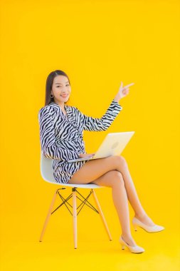 Güzel bir Asyalı kadın, sarı izole edilmiş arka planda dizüstü bilgisayar kullanıyor.