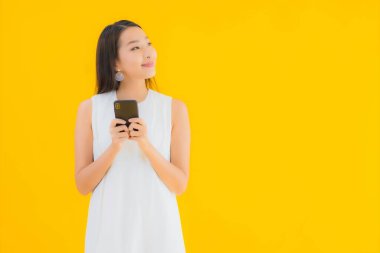 Sarı izole edilmiş arka planda akıllı cep telefonlu güzel Asyalı kadın portresi