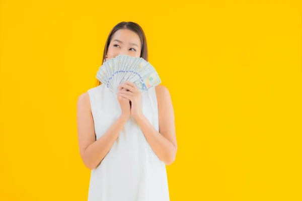 Portrait beautiful young asian woman with money cash on yellow isolated background