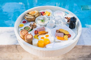 Kızarmış yumurta omletli, jambonlu, meyveli, sütlü kahveli ve yüzme havuzlu bir tepside yüzen kahvaltı.