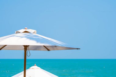 Plaj okyanusunun güzel tropik doğası çevresindeki beyaz şemsiye seyahat tatili için.