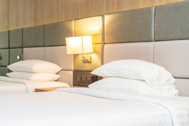 Yatak odasının içinde lamba süslemesi olan beyaz rahat yastık ve battaniye.