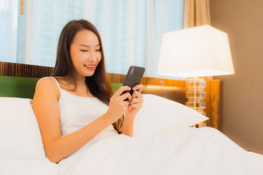 Güzel bir Asyalı kadın yatak odasının içinde akıllı cep telefonu kullanıyor.