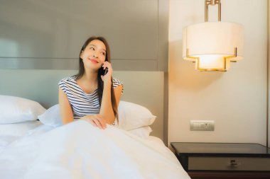 Güzel bir Asyalı kadın yatak odasının içinde akıllı cep telefonu kullanıyor.