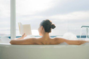 Güzel bir Asyalı kadının portresi. Banyo içinde beyaz bir küvette kitap okuyordu.