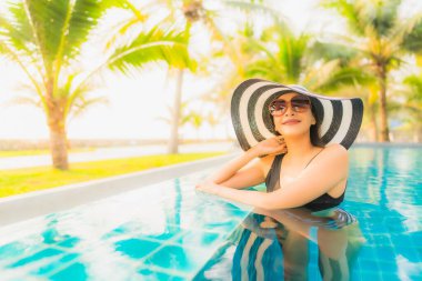 Güzel bir Asyalı kadın portresi, gün batımında palmiye ağacıyla birlikte havuz kenarında dinleniyor ya da tatil için gün doğumunda dinleniyor.