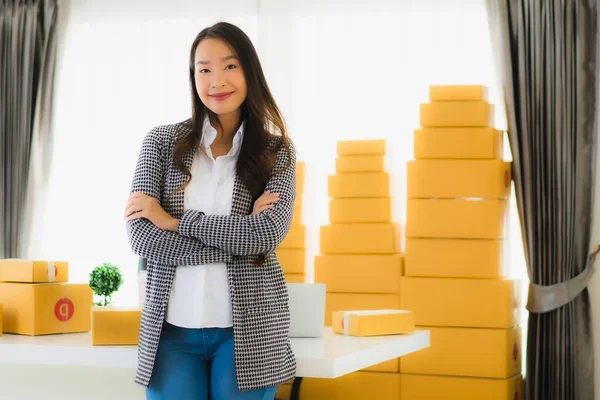 Portrait beautiful young asian business woman work from home with laptop mobile phone with cardboard box ready for shipping online shopping