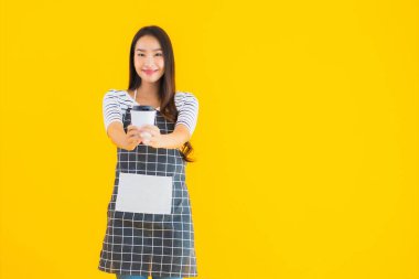 Güzel bir portre genç Asyalı kadın önlük giyer, gülümser ve sarı izole arka planda mutlu olur.