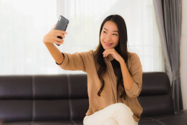 Güzel bir Asyalı kadın portresi. Kanepenin iç tarafında cep telefonu ya da kahve fincanı ile cep telefonu kullanıyor.