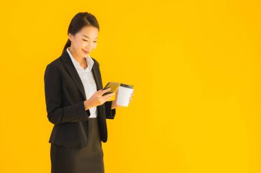 Portre güzel genç Asyalı kadın akıllı cep telefonu ve kahve fincanı ile izole edilmiş sarı arka planda