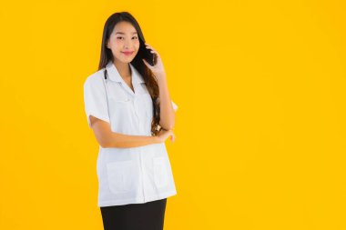 Güzel Asyalı genç doktor kadın sarı izole edilmiş arka planda akıllı cep telefonu kullanıyor.