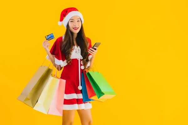 肖像画美しい若いアジアの女性は 黄色の隔離された背景に買い物袋の多くとクリスマス服の帽子を着用 — ストック写真