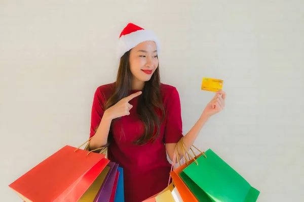 亚洲年轻貌美的女性头戴圣诞礼帽 头戴购物袋 头戴智能手机 头戴信用卡 — 图库照片