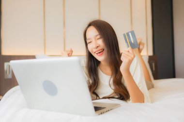 Güzel bir Asyalı kadın yatak odasının içinde dizüstü bilgisayar kullanıyor.