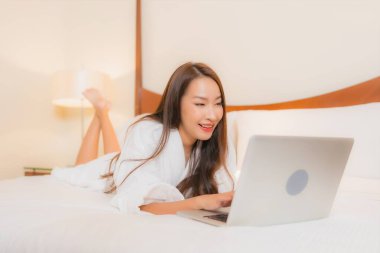 Güzel bir Asyalı kadın yatak odasının içinde dizüstü bilgisayar kullanıyor.