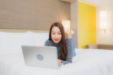 Güzel bir Asyalı kadın yatak odasının iç kısmında bilgisayar kullanıyor.