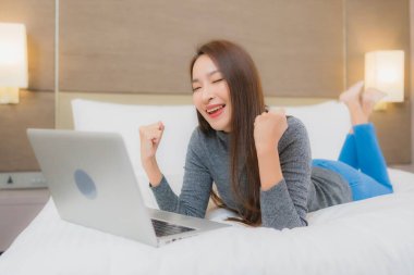 Güzel bir Asyalı kadın yatak odasının iç kısmında bilgisayar kullanıyor.