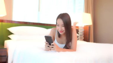 Yatakta akıllı telefon kullanan Asyalı güzel bir kadının görüntüleri.
