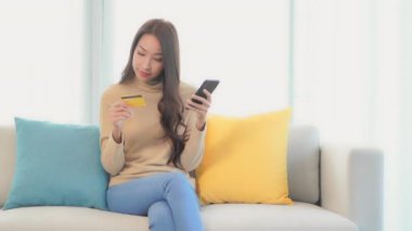 Güzel Asyalı bir kadının akıllı telefon ve kredi kartıyla e-alışveriş yaptığı görüntüler.