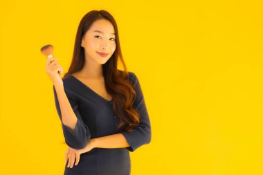 Sarı izole arkaplanda makyaj fırçası olan güzel bir Asyalı kadın portresi.