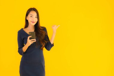Akıllı cep telefonlu güzel Asyalı kadın portresi ya da sarı izole edilmiş arka planda cep telefonu.