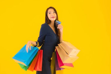 Portre güzel genç Asyalı kadın alışveriş çantası kredi kartı ve akıllı cep telefonu sarısı izole bir arka plan.