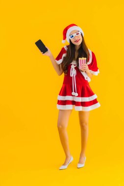 Güzel bir Asyalı kadın portresi patlamış mısır ve 3D gözlüklü noel şapkası takıyor sarı izole edilmiş arka planda film izlemeye hazır.