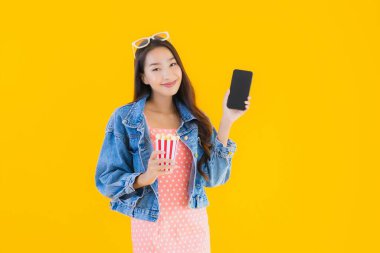 Güzel bir Asyalı kadın portresi telefon patlamış mısırı ve sarı izole edilmiş bir arka planda film izlemekten memnun.