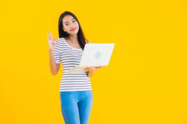 Güzel bir Asyalı kadın portresi çalışmak için dizüstü bilgisayar ya da defter kullanır ve sarı izole arka planda çalışır.