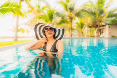 Güzel bir Asyalı kadın portresi, gün batımında palmiye ağacıyla birlikte havuz kenarında dinleniyor ya da tatil için gün doğumunda dinleniyor.