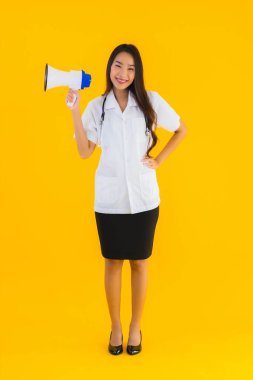 Güzel bir Asyalı genç doktor portresi. Sarı izole arka planda megafon kullanıyor.