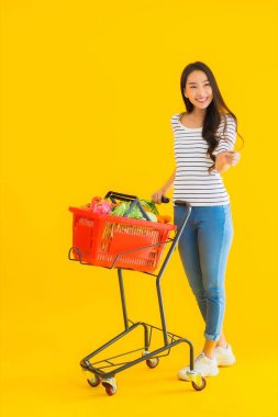 Sarı izole edilmiş arka planda, süpermarketten alışveriş sepeti taşıyan güzel Asyalı kadın portresi