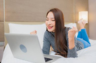Güzel bir Asyalı kadın yatak odasının iç kısmında bilgisayar kullanıyor.