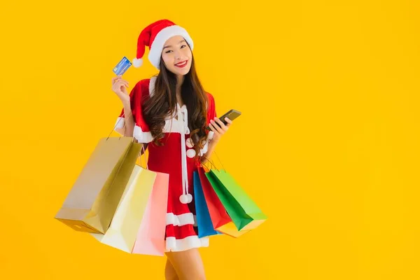 肖像画美しい若いアジアの女性は 黄色の隔離された背景に買い物袋の多くとクリスマス服の帽子を着用 — ストック写真