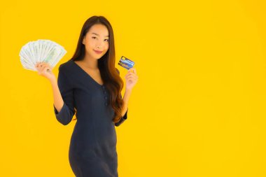 Güzel bir Asyalı kadın portresi. Parası ve kredi kartıyla izole edilmiş sarı arka plan.