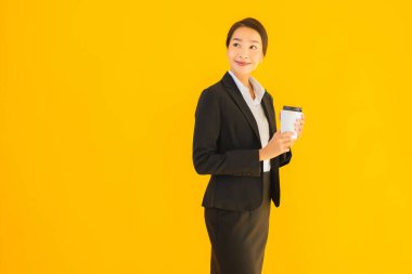 Portre güzel genç Asyalı kadın akıllı cep telefonu ve kahve fincanı ile izole edilmiş sarı arka planda