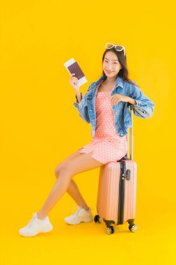Çantalı güzel Asyalı kadın. Pasaportu ve sarı izole bir arka planda bilet.