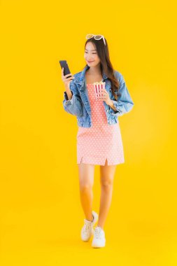 Güzel bir Asyalı kadın portresi telefon patlamış mısırı ve sarı izole edilmiş bir arka planda film izlemekten memnun.