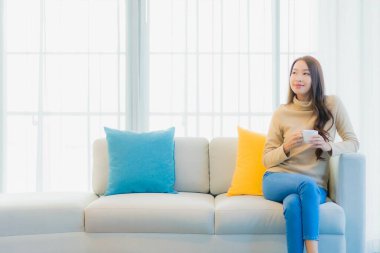Oturma odasındaki kanepede kahve fincanı taşıyan güzel Asyalı kadın portresi.