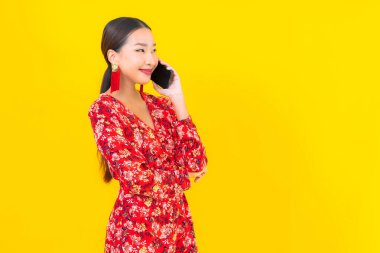 Güzel bir Asyalı kadın. Sarı arka planda akıllı cep telefonu kullanıyor.