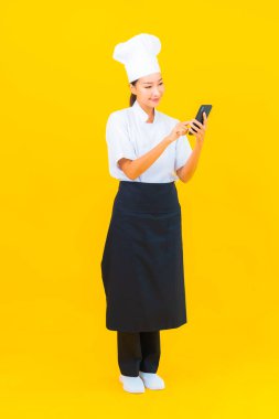 Sarı izole edilmiş arka planda akıllı cep telefonlu güzel Asyalı şef kadın portresi.