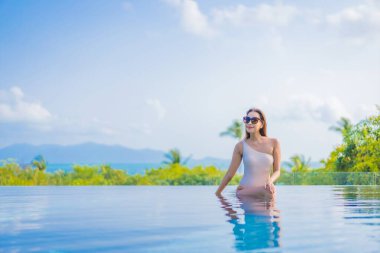 Güzel bir Asyalı kadın portresi gezide deniz manzaralı açık havuzda yüzüyor.
