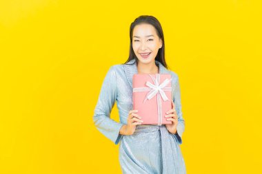 Asyalı güzel bir kadının portresi. Sarı arka planda kırmızı hediye kutusuyla gülümsüyor.