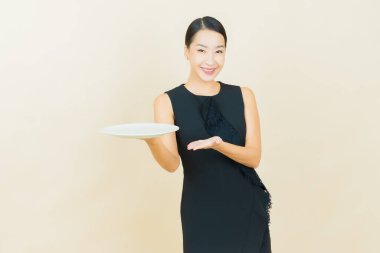 Güzel Asyalı bir kadının portresi. Arka planda boş tabak tabağıyla gülümsüyor.