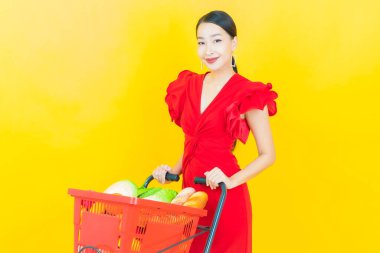 Renkli arka planda süpermarketten alınmış market sepetiyle gülümseyen güzel Asyalı kadın portresi.