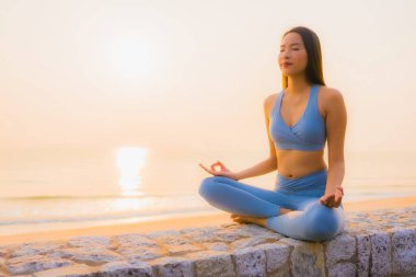 Genç Asyalı kadının portresi sağlık için gün doğumunda deniz kıyısı okyanusunda meditasyon yapıyor.